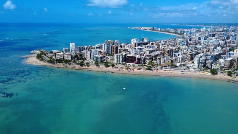 Toma aérea de drone desde el mar hacia el barrio de Ponta Verde. Mar turquesa, playa con palmeras y edificios al fondo