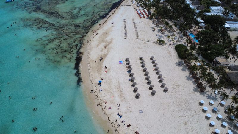 Vista aérea de Playa Norte en Isla Mujeres, con arena blanca, aguas cristalinas y sombrillas alineadas junto al mar turquesa
